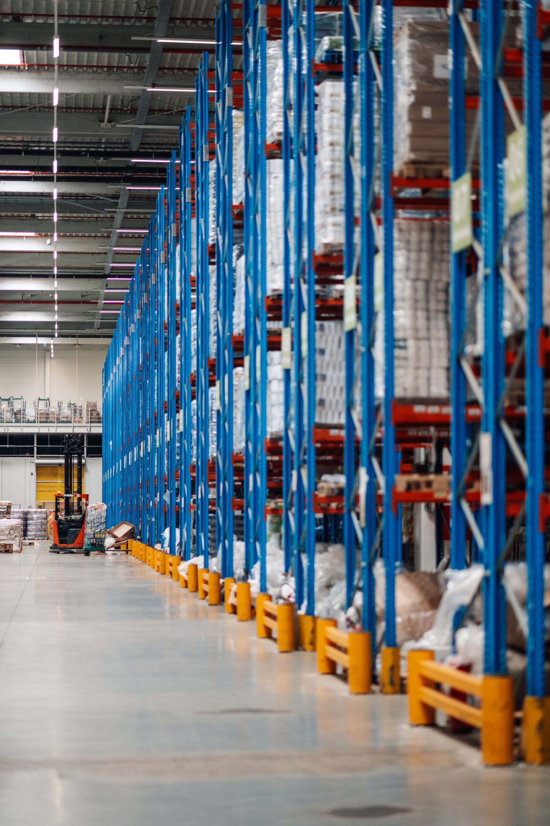 Forklift truck moving goods in large distribution warehouse with high shelves full of packages